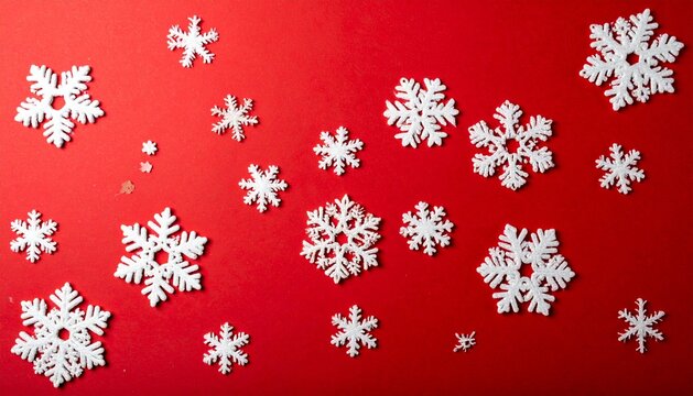 A flat lay composition of various white snowflake ornaments scattered randomly across a vibrant, solid red background. A classic winter and Christmas holiday pattern with ample room for text.