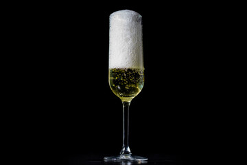 Pouring champagne into a wineglass. Close-up of champagne splash in glass. Sparkling champagne wine with fizz on black background. Sparkling champagne with golden shine in wineglass.