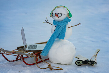 Snowman browsing internet in snowy field. Remote online work winter concept. Snowman doing remote work in winter landscape. Snow man office setup outside. Funny snowman working on computer.