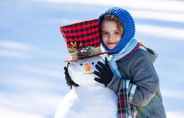 Child hug snowman. Child play with snowman in snow field. Kids winter activity. Child enjoying winter creativity in snowy field. Child decorating snowman. Kid building snowman. Kids winter fun.