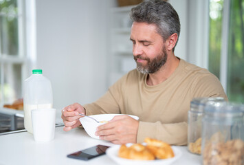Middle aged Man eat breakfast in the kitchen on a morning. Guy eat vegetables for a healthy meal in his kitchen in morning. Man eat healthy food in kitchen. Morning breakfast in the modern kitchen.