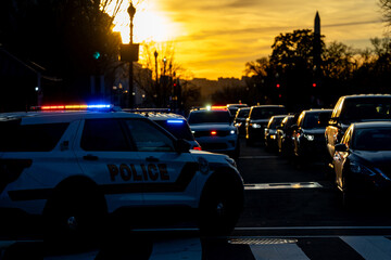 Police car stops traffic at sunset. Red and blue lights flash intensely. Security units follow protocol. Law enforcement holds the line. Capitol zone remains secure.