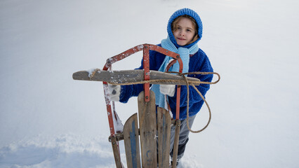 Child with sled play in winter snowy field. Winter kid portrait Kid enjoying snowy day. Winter kids fun with vintage sled outdoors. Kid play in snow. Childhood in winter.