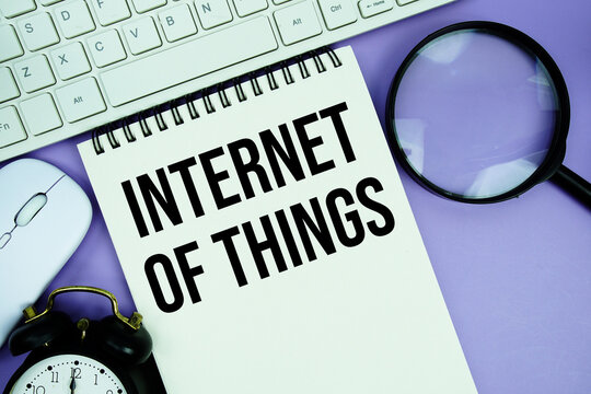 Notepad with the text "Internet of Things" and white keyboard, wireless mouse, magnifying glass and alarm clock