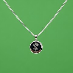 A close-up of a silver necklace with a round pendant featuring a rose design, set against a vibrant green background