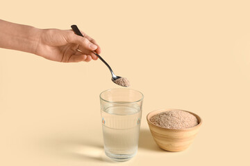 Female hand adding psyllium husk into glass of water on beige background