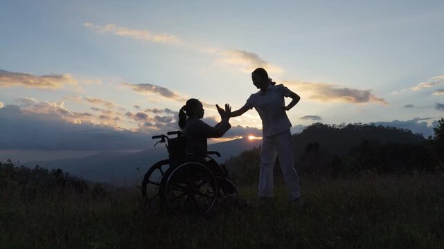 Silhouette elderly woman in wheelchair dancing with his care helper on mountain sunset. Psychological medication  treatment concept