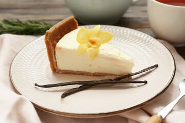 Plate of sweet cheesecake slice with vanilla flower and sticks on wooden background