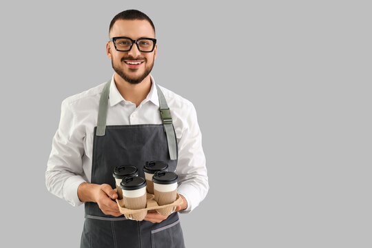 Young male barista with paper cups of coffee on grey background - Powered by Adobe