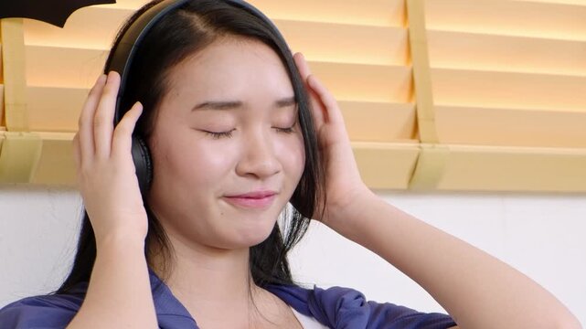 Young woman enjoying music while wearing headphones in a serene indoor setting with warm lighting and closed eyes exuding relaxation and bliss