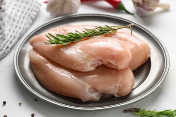 Plate with raw chicken breast and different spices on white background