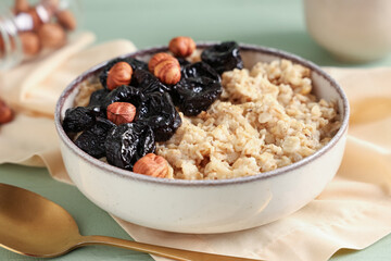 Bowl of tasty oatmeal with prunes and hazelnuts, closeup