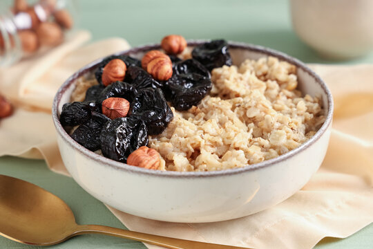 Bowl of tasty oatmeal with prunes and hazelnuts, closeup