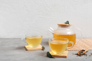 Glass cups and teapot of hot green tea with dried leaves on grey table