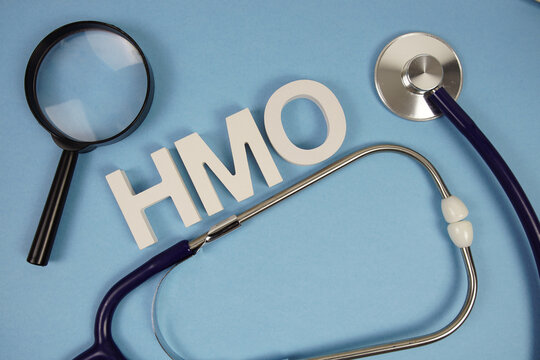 HMO abbreviation of Health Maintenance Organization alphabet letters with magnifying glass and stethoscope on blue background