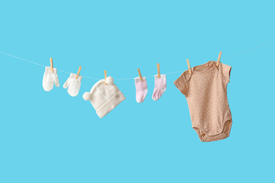 Baby bodysuit with accessories hanging on rope against blue background - Powered by Adobe