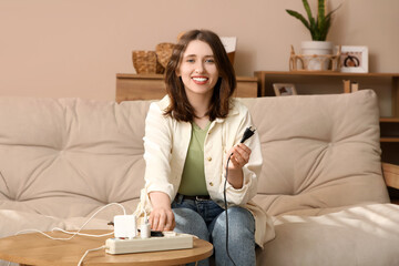 Young woman with plug and extension cord sitting on sofa at home. National Day of Unplugging
