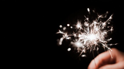 Sparkling Festive Celebration: Close-Up of a Hand Holding a Lit Sparkler Against a Dark Background