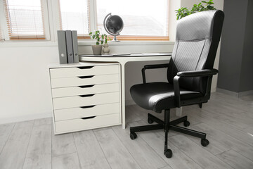 Comfortable workplace with leather black chair near window in room, closeup
