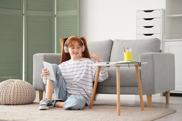 Little redhead girl with tablet computer studying online at home