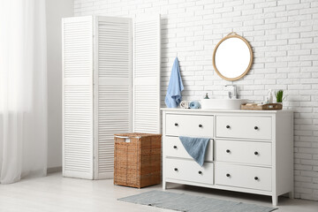Interior of stylish bathroom with sink, dresser and folding screen