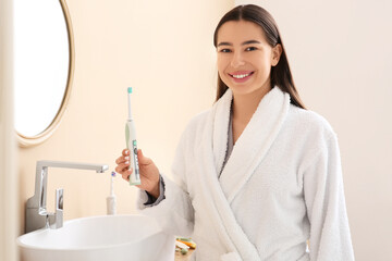 Morning of happy young woman with electric toothbrush in bathroom