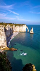 A coastal landscape featuring towering white cliffs, an archway, a pebbled beach, and crystal blue water under a bright sky