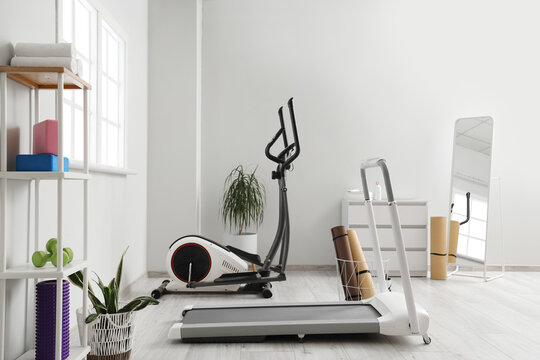 Interior of stylish gym with modern treadmill, elliptical machine and sports equipment