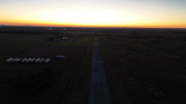 A cinematic aerial shot approaches the end of a abandoned decommissioned runway at Markham Airport during sunset, with a distant Toronto skyline visible on the horizon