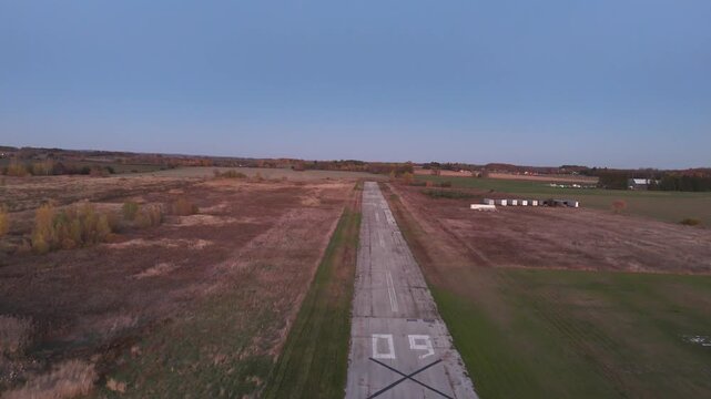 A cinematic aerial shot moves forward along the abandoned Markham Airport runway while simultaneously elevating, revealing the expansive, unused airfield and distant autumn landscape