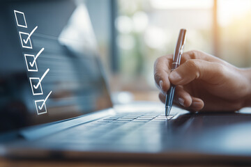 A hand holding a pen is writing on a laptop, with a visible checklist on the screen, suggesting organization and productivity.