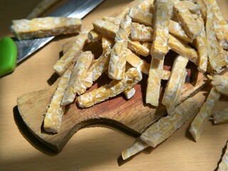 Raw tempeh slices in stick form on a wooden cutting board. Preparing to cook tempeh. Preparing to eat tempeh.