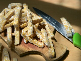 Raw tempeh slices in stick form on a wooden cutting board. Preparing to cook tempeh. Preparing to eat tempeh. Artistic food photos.