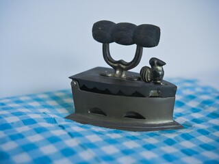 An antique brass iron exposed to sunlight on blue patterned fabric. An old household ironing tool.