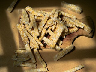 Raw tempeh slices in stick form on a wooden cutting board. Preparing to cook tempeh. Preparing to eat tempeh. Artistic food photos.