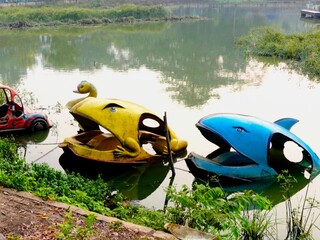 A broken paddle boat on the shore of an amusement park lake. Damaged park facilities. Water attractions at the amusement park.