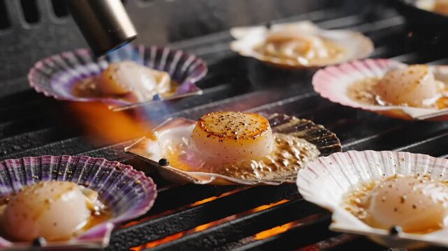 Seared scallops being torched on a grill in their shells for gourmet restaurant cuisine