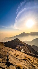 A scenic vista shows a mountain range bathed in the golden light of the setting sun, with scattered clouds in the vast sky
