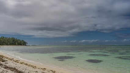 A secluded tropical beach with no people. Dry algae on white sand. A calm turquoise ocean. Green vegetation in the distance. Blue sky, clouds. Mauritius. Île aux Cerfs 