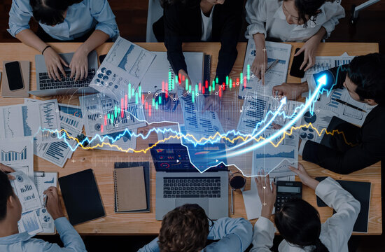 A diverse business team engages in financial analysis, utilizing charts and advanced technology for productive discussions and strategic planning in a modern office setting. Scalp