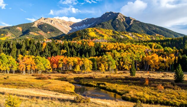 A scenic mountainous landscape captures autumnal colors. Yellows, reds, and greens meet a snow-capped peak. A small stream winds through