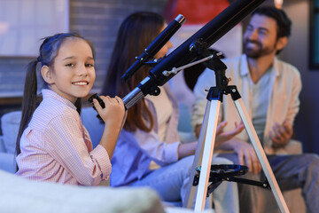 Little girl with her parents and telescope at home in evening