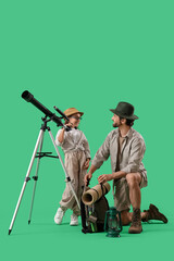 Fototapeta premium Male adventurer with his little daughter and telescope on green background