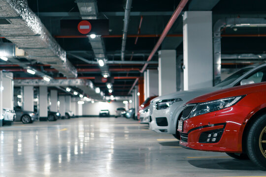 Row of parked cars in a modern underground parking garage with bright ceiling lights and clean concrete floor. Urban infrastructure interior suitable for themes of real estate, security, transportatio