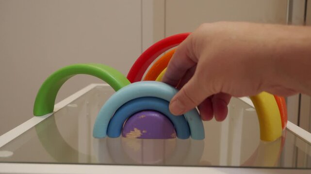 Wooden rainbow stacking blocks are moved around on a glass table. The blocks make a series of light, hollow clicks and clacks as they touch each other and the hard surface.