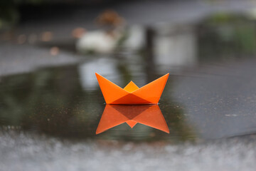 Origami boat floating on shallow water puddle outdoors, closeup