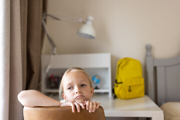Thoughtful young girl sitting in a bedroom near a study desk