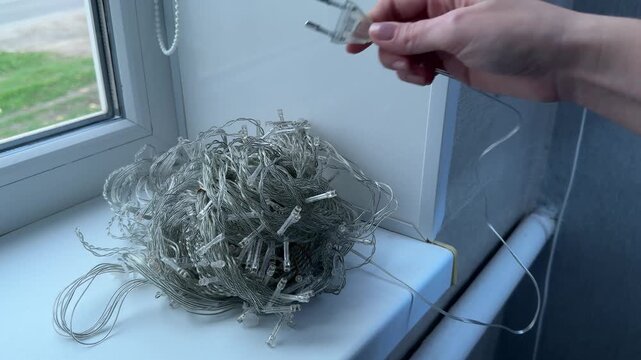 Female hand unplugging glowing string lights from wall socket at home