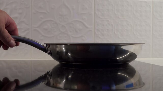 A metal frying pan is placed on a glass cooktop with a heavy clank. The hard surfaces create a solid, resonant sound.