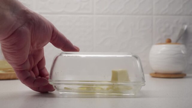 A glass butter dish is placed on a countertop with a solid thud. The hard glass makes a clear, sharp sound against the surface.